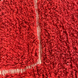 May include: Close-up of a vibrant red, textured rug. The rug has a thick, plush pile, with a lighter, striped border. The texture suggests a soft, comfortable feel. The rug is a solid red color.