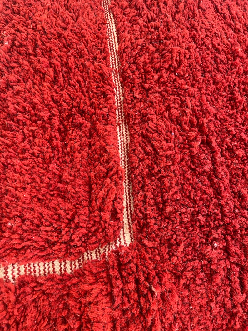May include: Close-up of a vibrant red, textured rug. The rug has a thick, plush pile, with a lighter, striped border. The texture suggests a soft, comfortable feel. The rug is a solid red color.