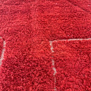 May include: A close-up of a red, textured rug with a plush, shaggy appearance. The rug has a geometric pattern with white stripes. The rug is made of a soft material and is suitable for a living room or bedroom.