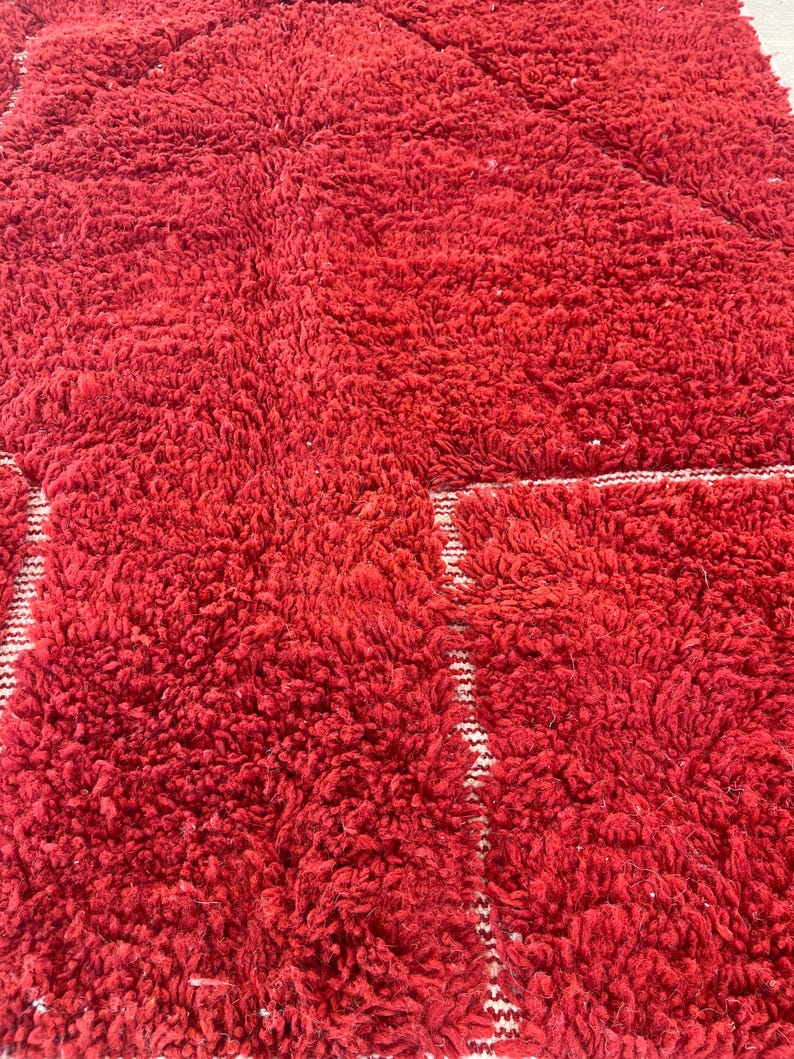 May include: A close-up of a red, textured rug with a plush, shaggy appearance. The rug has a geometric pattern with white stripes. The rug is made of a soft material and is suitable for a living room or bedroom.