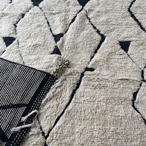 May include: A white and black geometric patterned rug with a fringe border. The rug has a fluffy texture.