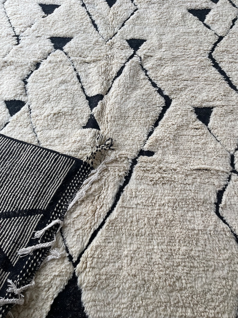 May include: A white and black geometric patterned rug with a fringe border. The rug has a fluffy texture.