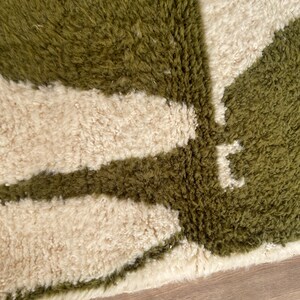 Pode incluir: Close-up de um tapete felpudo verde e branco com um padr&atilde;o geom&eacute;trico. O tapete tem uma pilha grossa e uma textura macia.