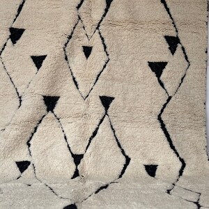 May include: A white and black geometric patterned rug with a fluffy texture. The rug has a diamond pattern with black triangles.