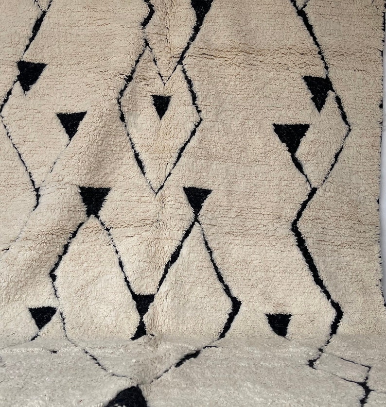 May include: A white and black geometric patterned rug with a fluffy texture. The rug has a diamond pattern with black triangles.