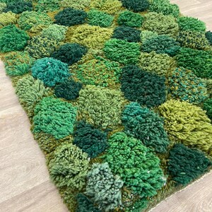 May include: A hand-tufted rug with a textured design in shades of green. The rug has a pattern of raised, rounded shapes, creating a 3D effect. The colour palette includes light, medium, and dark greens, giving it a natural, organic appearance.