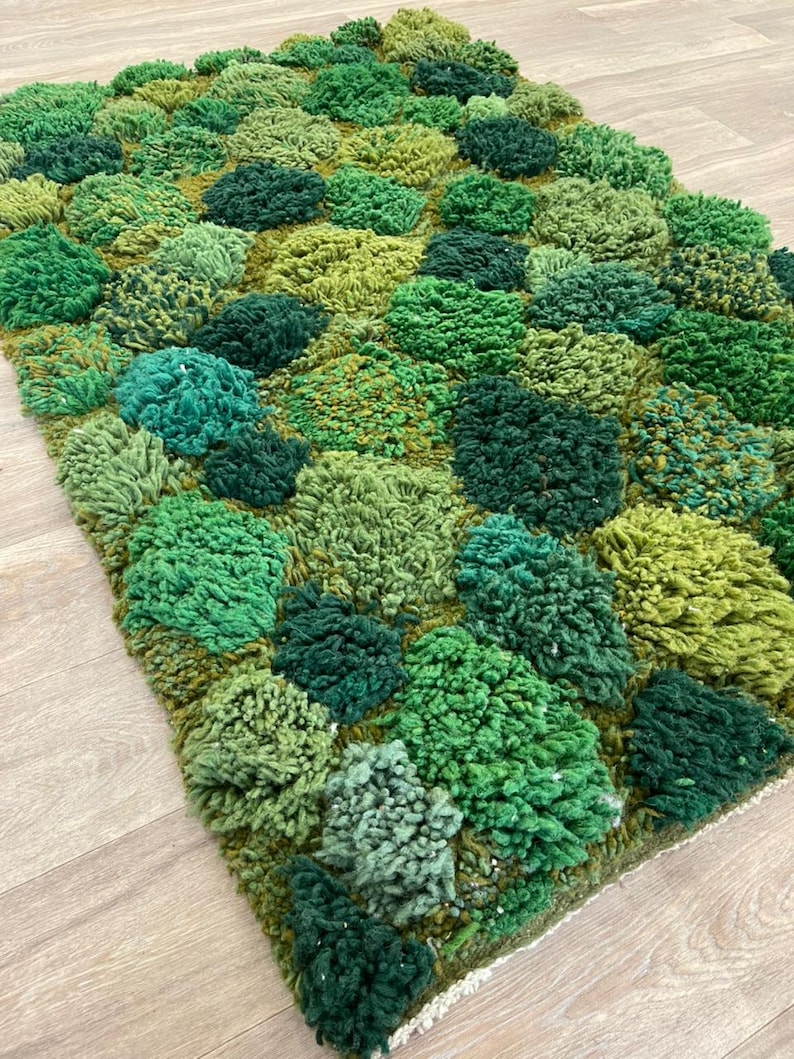 May include: A hand-tufted rug with a textured design in shades of green. The rug has a pattern of raised, rounded shapes, creating a 3D effect. The colour palette includes light, medium, and dark greens, giving it a natural, organic appearance.