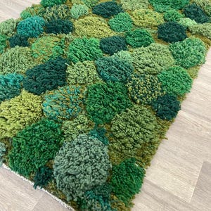 May include: A green textured rug with a tufted design. The rug features a pattern of raised, rounded shapes, creating a three-dimensional effect. The color palette ranges from light to dark greens, adding depth and visual interest to the floor covering.