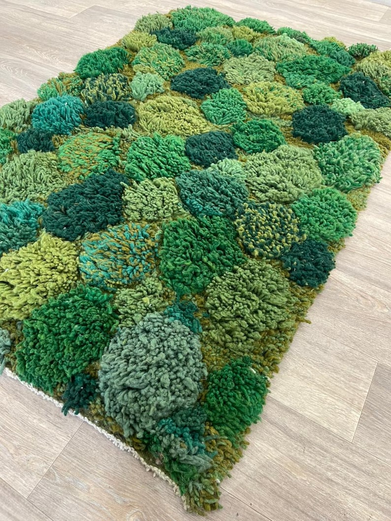 May include: A green textured rug with a tufted design. The rug features a pattern of raised, rounded shapes, creating a three-dimensional effect. The color palette ranges from light to dark greens, adding depth and visual interest to the floor covering.