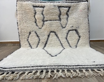 Könnte beinhalten: Weißer und schwarzer marokkanischer Teppich mit geometrischem Muster und Fransen. Der Teppich ist aus Wolle und hat eine weiche, flauschige Textur.