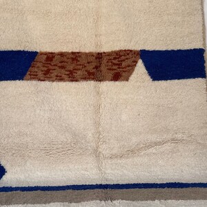 May include: A white rug with blue and brown geometric patterns. The rug has a soft, fluffy texture.