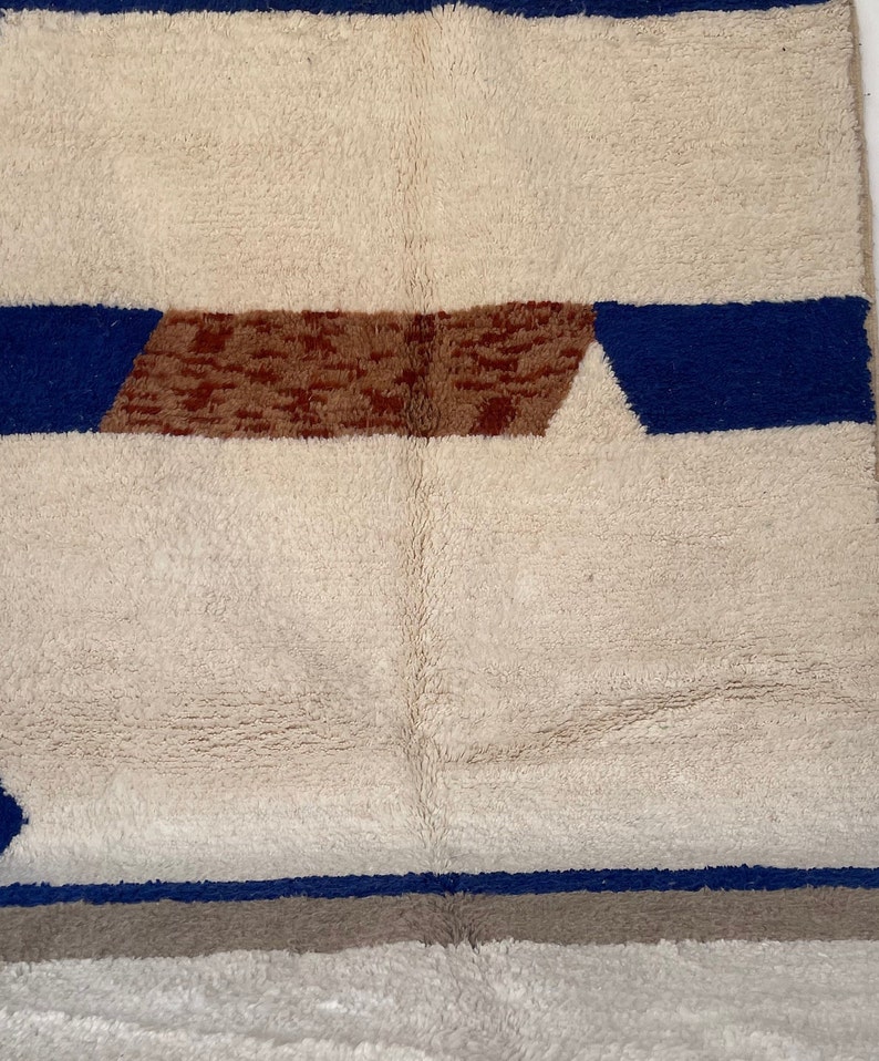 May include: A white rug with blue and brown geometric patterns. The rug has a soft, fluffy texture.