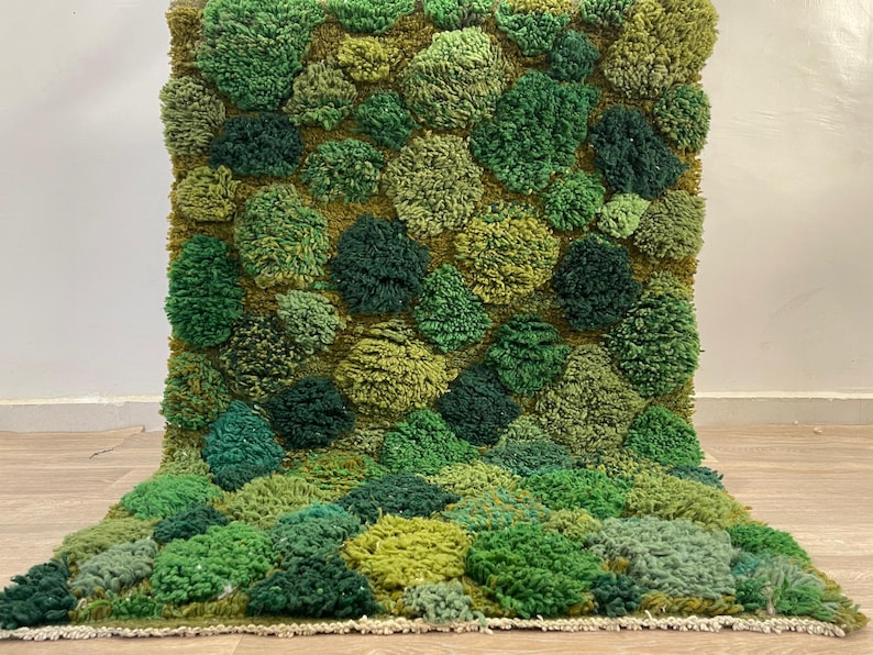 May include: A green textured rug with a design reminiscent of a mossy landscape. The rug features a pattern of raised, rounded shapes in various shades of green. The color palette includes light and dark greens, with a hint of yellow, creating a natural look.