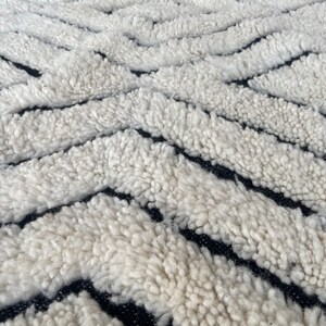 May include: Close-up of a white and black patterned rug with a fluffy texture. The rug has a geometric design with thick white stripes and thin black stripes.