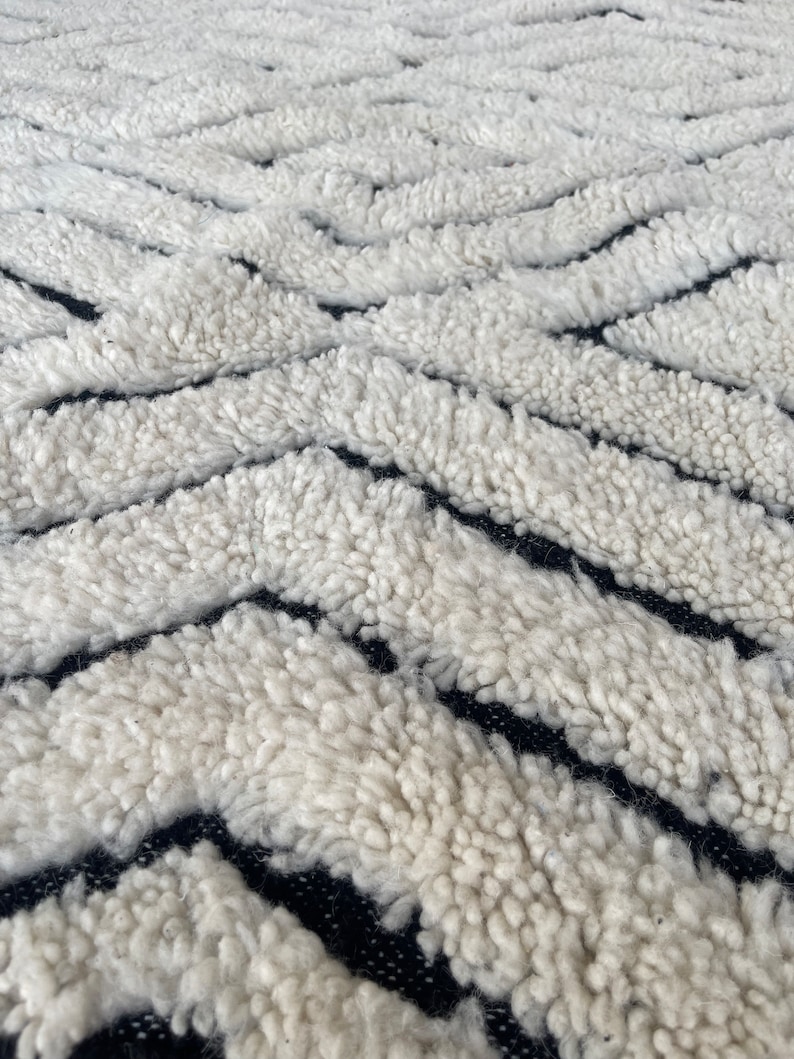 May include: Close-up of a white and black patterned rug with a fluffy texture. The rug has a geometric design with thick white stripes and thin black stripes.