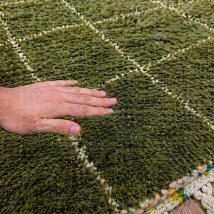 May include: A close-up of a green rug with a diamond pattern. The rug has a textured, shaggy appearance with white lines forming the diamond grid. The edge of the rug has a fringe detail.