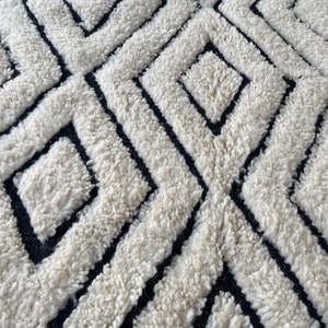 May include: A white and black geometric patterned rug with a fluffy texture. The rug has a black border with a white trim.