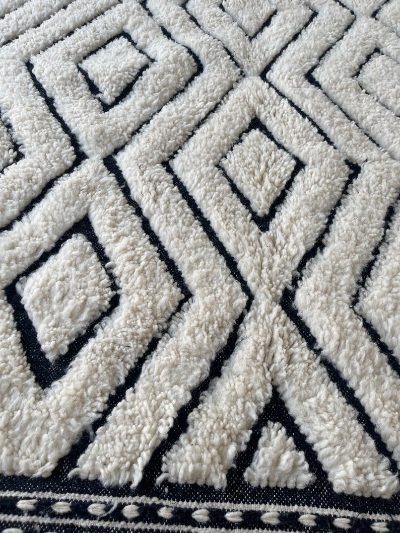May include: A white and black geometric patterned rug with a fluffy texture. The rug has a black border with a white trim.