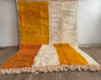 May include: A rectangular rug with a geometric pattern in shades of white, orange, and yellow. The rug has a fringe border.
