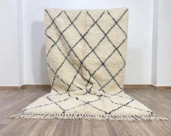 May include: A rectangular area rug featuring a thick, cream-colored pile with a repeating black diamond grid pattern. The rug has a textured, shaggy surface and is finished with long, cream-colored fringe tassels along the bottom edge.