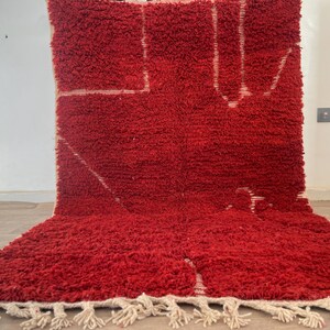 May include: A vibrant red rug with a thick, textured pile. The rug features a geometric design in white, with a fringe along the bottom edge. The rug is a bold statement piece for any room.