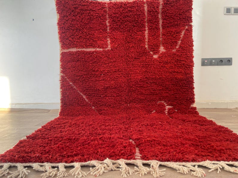 May include: A vibrant red rug with a thick, textured pile. The rug features a geometric design in white, with a fringe along the bottom edge. The rug is a bold statement piece for any room.
