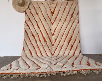 Puede incluir: Una alfombra marroquí blanca y naranja con un patrón de chevron. La alfombra tiene un borde de flecos.