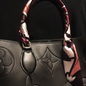 May include: Black leather handbag with a patterned scarf wrapped around the handle. The handbag has a large embossed monogram pattern.