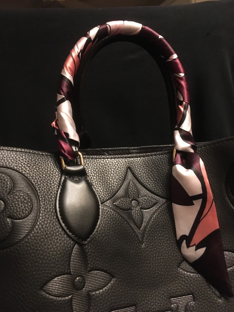 May include: Black leather handbag with a patterned scarf wrapped around the handle. The handbag has a large embossed monogram pattern.