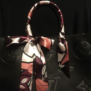 May include: A black leather handbag with a floral patterned scarf tied around the handles. The scarf is in shades of pink, white, and burgundy.