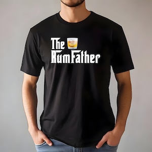 May include: Black t-shirt with the text "The RumFather" in white, accompanied by a graphic of a cocktail. The design resembles a classic movie title. The shirt is made of a soft material.
