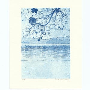 May include: A blue and white print of a landscape featuring a body of water, mountains, and a tree branch with leaves. The print is on a cream-colored paper. The artist's signature and edition number are visible.