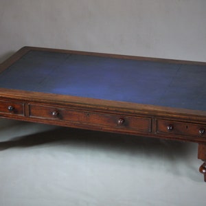 Op de afbeelding: Een rechthoekige houten salontafel met een donkerblauwe leren bovenkant. De tafel heeft vier lades met ronde knoppen en staat op vier gedraaide poten. Het hout heeft een rijke, warme bruine tint.
