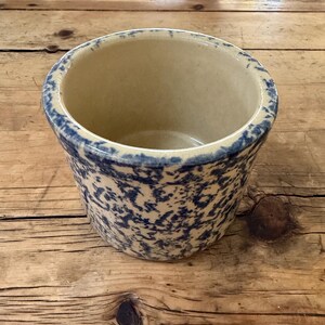 May include: A cylindrical stoneware crock featuring a cream-coloured interior and a blue sponge-painted exterior pattern. The vessel has a wide, open top with a thick, rounded rim and a smooth, glazed finish throughout the entire ceramic surface.