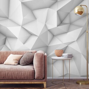 Könnte beinhalten: Ein altrosa Sofa mit einem hellbeigen Kissen und einem dunkelgrauen Kissen, neben einem kleinen runden Tisch mit einer Holzschale und einem Stapel Bücher, einer hohen goldenen Stehlampe und einer weißen geometrischen Wand.