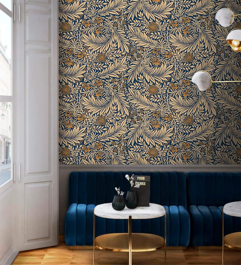 May include: A blue velvet sofa with gold trim sits in front of a wall covered in a blue and gold floral wallpaper. The sofa is accented with two small black vases and a book titled "Food & Drinks".