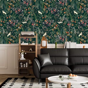 K&ouml;nnte beinhalten: Eine dunkelgr&uuml;ne Tapete mit einem sich wiederholenden Muster aus V&ouml;geln, Bl&auml;ttern und Blumen. Die Tapete ist in einem Wohnzimmer mit einem schwarzen Ledersofa, einem Holzregal und einem Couchtisch zu sehen.