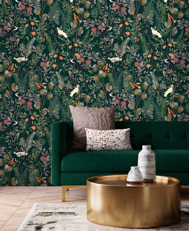 K&ouml;nnte beinhalten: Ein gr&uuml;nes Samtsofa mit zwei Kissen steht vor einer gr&uuml;nen Tapete mit Blumenmuster. Ein runder goldener Couchtisch mit geh&auml;mmerter Oberfl&auml;che steht vor dem Sofa. Zwei wei&szlig;e Keramikvasen stehen auf dem Tisch.