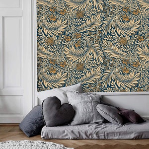 May include: A bedroom with a blue and cream floral wallpaper. The bed is covered with a gray blanket and has several gray pillows. A white knitted rug is on the floor.