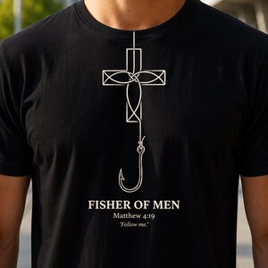 Peut inclure: Un t-shirt noir arborant un graphisme en lignes blanches représentant une croix intégrée à un hameçon. Sous le motif, le texte indique : FISHER OF MEN, Matthew 4:19, 'Follow me.' Le design est centré sur la poitrine du vêtement.