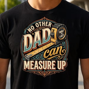 May include: A black t-shirt featuring a graphic design with a yellow tape measure and the text NO OTHER DAD can MEASURE UP and BUILT TO LAST. The design is framed by a decorative border with orange, blue, and cream colours on a dark background.