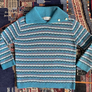 May include: A vintage blue knit sweater with a wide collar and button detail. The sweater features horizontal stripes in white, red, and black. The sleeves and collar are a solid blue. The label reads "Vivianne Lee".