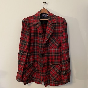 May include: A red, black, and green plaid blazer with two front pockets and a single chest pocket. The blazer has a notched lapel and three black buttons. The jacket is hanging on a wooden hanger.
