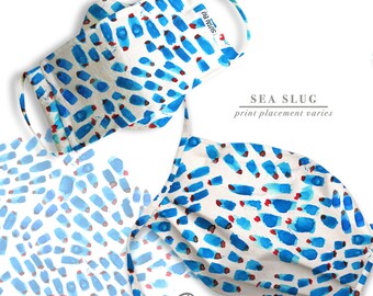 May include: Two white face masks with blue and red watercolor-style abstract patterns. The masks are made by Sutalbu and have the text "SEA SLUG print placement varies" on the white background.