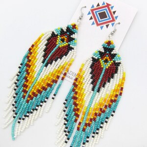May include: A pair of long, beaded earrings with a geometric pattern in shades of turquoise, red, yellow, black, and white. The earrings are made of seed beads and have a fringe-like design.