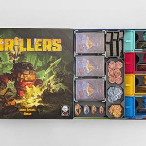 May include: The board game Drillers with a box cover featuring a red mechanical drill machine and the title text. The open box contains organised game components including three stacks of cards, grey trays with copper and silver tokens, and four coloured plastic bins holding small figurines.