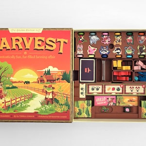 Puede incluir: Caja de juego de mesa abierta, titulada "HARVEST: Golden Edition". La ilustración de la caja muestra una escena de granja. En el interior, hay fichas de animales, cartas y piezas de juego de madera, todo ordenado en una bandeja de almacenamiento marrón.