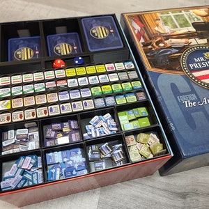 May include: A black and red organizer with multiple compartments filled with small game pieces. The organizer is open and next to a blue box with the text "Mr. President The American Presidency 2001-2021 Game Design by Gene Beley".