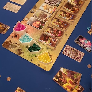 Peut inclure: Un plateau de jeu avec des gemmes color&eacute;es et des cartes. Le plateau est en bois et a un sch&eacute;ma de couleurs brun et beige. Les cartes sont de couleurs diff&eacute;rentes et ont des images de personnes et d'animaux dessus. Il y a aussi de petits contenants blancs avec des gemmes &agrave; l'int&eacute;rieur.