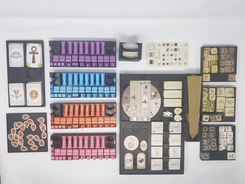May include: A black foam insert with compartments for organizing game pieces. The insert includes compartments for small tokens, dice, and cards. The insert is designed for a board game.